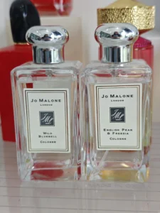 A side-by-side visual comparison of a traditional luxury designer peony perfume bottle and a factory-direct blush suede fragrance alternative.
