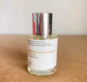 Side-by-side comparison of a traditional $300 luxury orchid and sandalwood perfume bottle versus a factory-direct USA lab formulation.